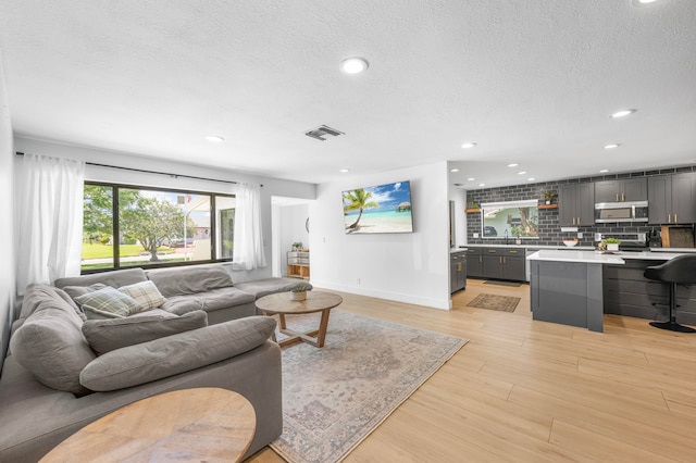 living room featuring a textured ceiling, light wood-type flooring, and sink