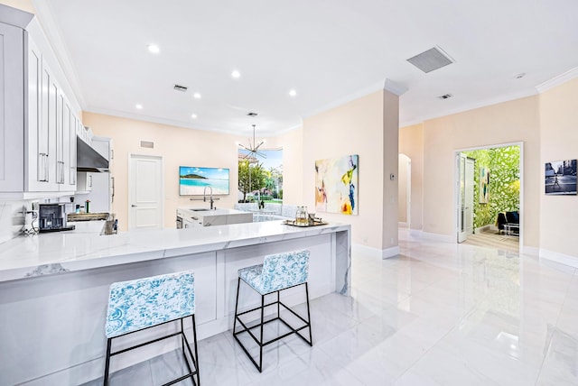 kitchen with white cabinets, crown molding, light stone countertops, kitchen peninsula, and a breakfast bar area