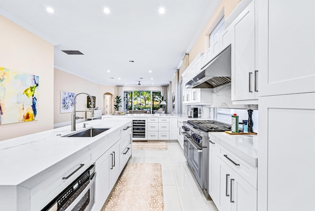 kitchen with high end range, white cabinets, wine cooler, and sink