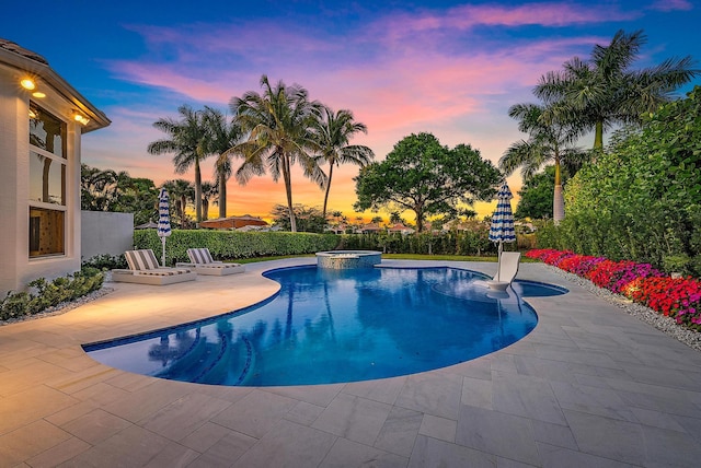 pool at dusk featuring a patio area and an in ground hot tub