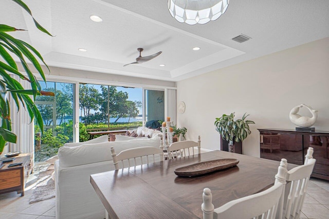 tiled dining area featuring a tray ceiling, a textured ceiling, and ceiling fan