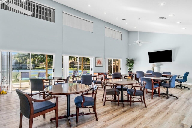 dining room featuring a towering ceiling, light hardwood / wood-style flooring, and ceiling fan