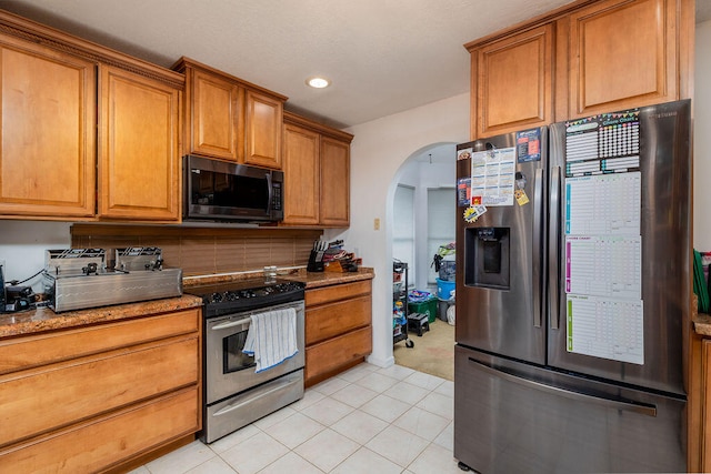 kitchen featuring light stone countertops, stainless steel appliances, decorative backsplash, and light tile patterned floors