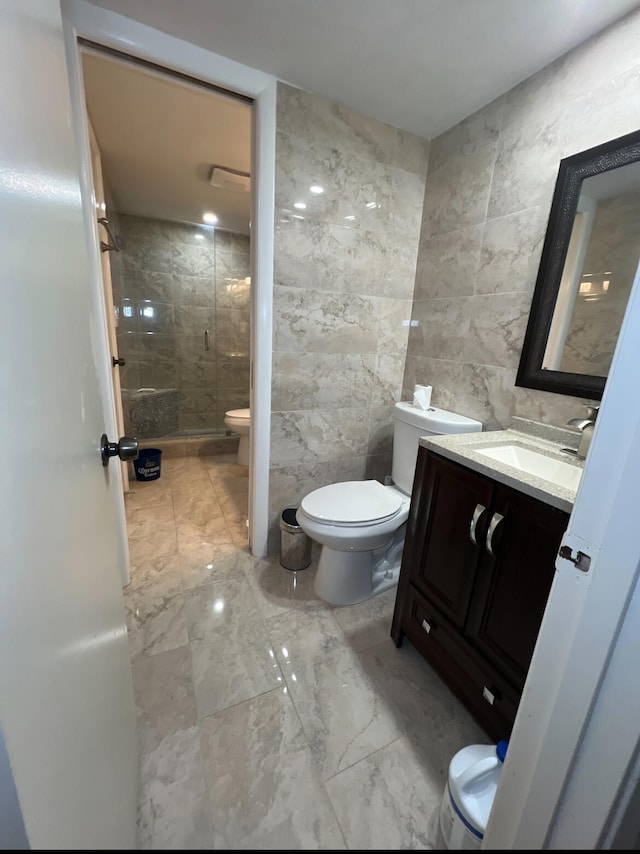 bathroom with a shower with door, vanity, toilet, and tile walls