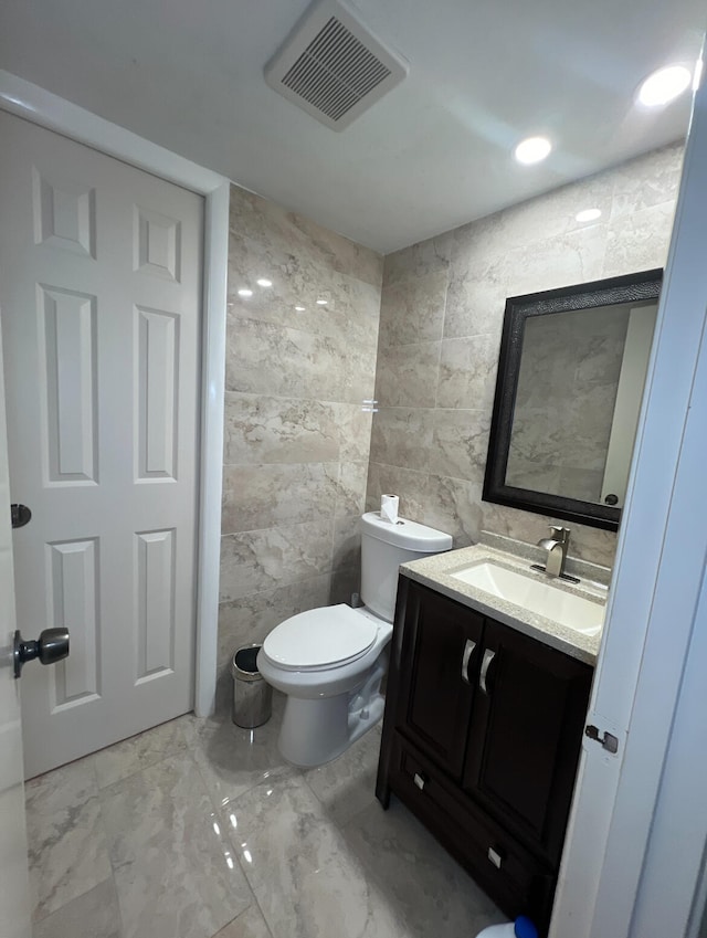 bathroom featuring toilet, vanity, and tile walls