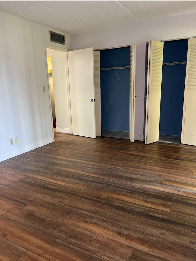 unfurnished bedroom with dark hardwood / wood-style floors and two closets