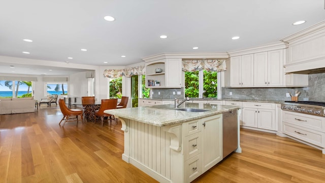 kitchen featuring sink, appliances with stainless steel finishes, light stone counters, an island with sink, and light wood-type flooring