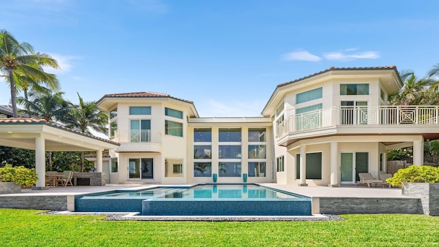 back of house with a balcony, a pool with hot tub, a patio, and a lawn