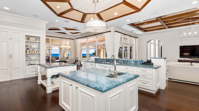 kitchen featuring kitchen peninsula, pendant lighting, a center island with sink, and dark stone countertops