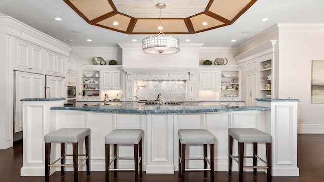 kitchen with a breakfast bar, white cabinetry, crown molding, and dark stone counters