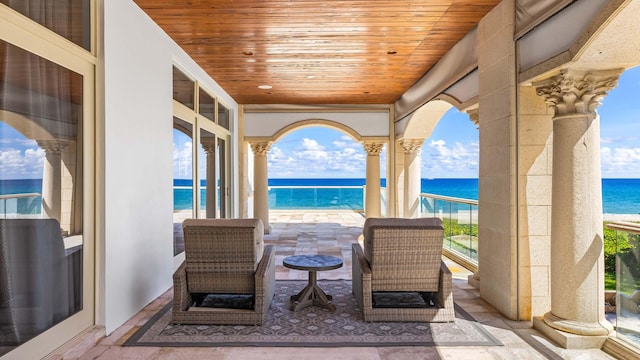 view of patio with a balcony, a water view, and a beach view