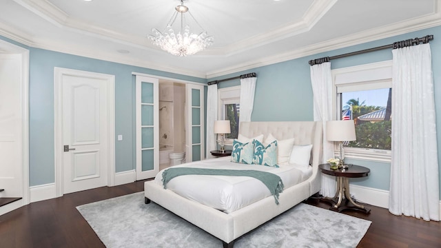 bedroom with ensuite bath, dark wood-type flooring, a raised ceiling, a notable chandelier, and ornamental molding