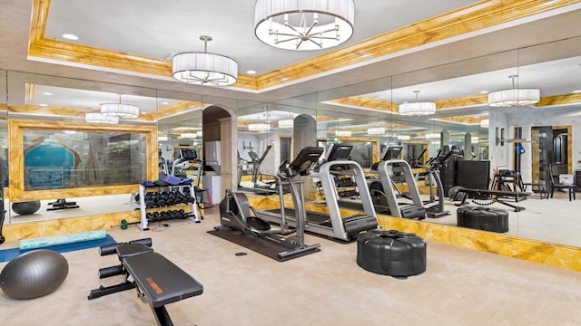 gym with a tray ceiling, crown molding, and a chandelier