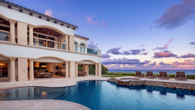 pool at dusk featuring an in ground hot tub and a patio