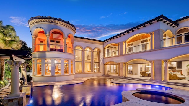 back house at dusk featuring a patio, a balcony, and a pool with hot tub