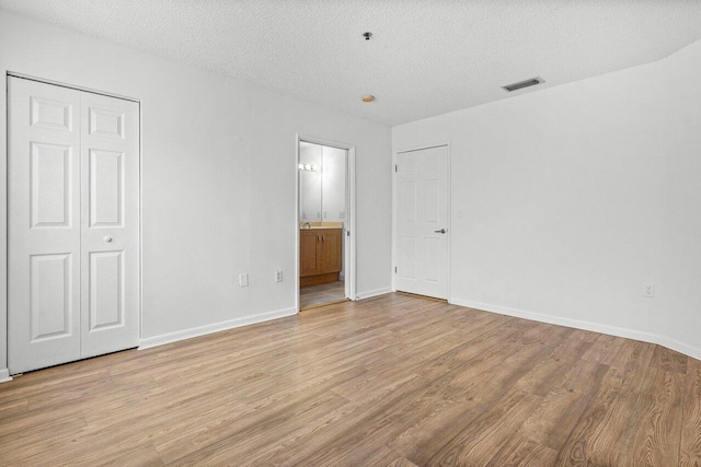 unfurnished bedroom featuring light hardwood / wood-style floors, a textured ceiling, a closet, and ensuite bath