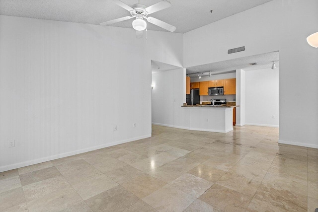 unfurnished living room with a towering ceiling, a textured ceiling, and ceiling fan