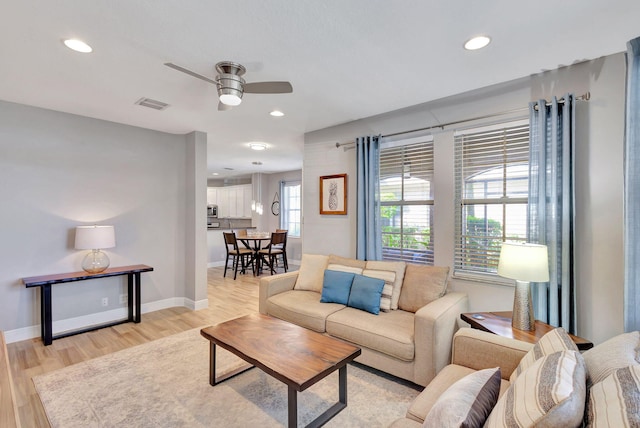 living room with light wood-type flooring, ceiling fan, and a healthy amount of sunlight