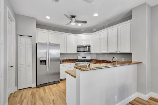 kitchen with white cabinetry, kitchen peninsula, appliances with stainless steel finishes, and dark stone counters