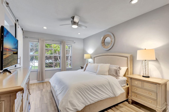 bedroom featuring ceiling fan, a barn door, and light hardwood / wood-style floors