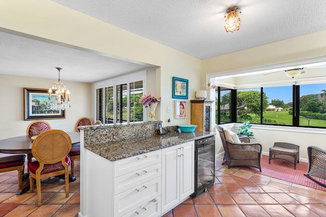 kitchen with dark stone counters, white cabinetry, wine cooler, hanging light fixtures, and a textured ceiling