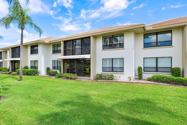 back of property with a lawn, stucco siding, and a tiled roof