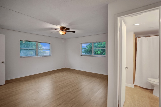 unfurnished bedroom with ceiling fan, ensuite bath, a textured ceiling, and light hardwood / wood-style floors