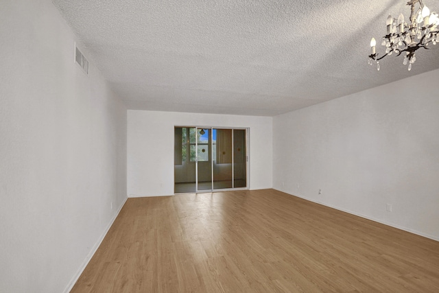 unfurnished room featuring a textured ceiling, hardwood / wood-style flooring, and an inviting chandelier