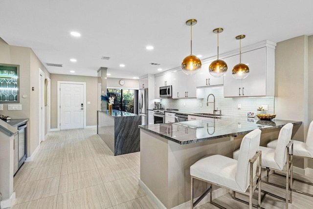 kitchen featuring appliances with stainless steel finishes, dark stone countertops, pendant lighting, white cabinets, and sink