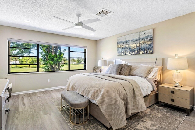 bedroom with a textured ceiling, ceiling fan, and light hardwood / wood-style flooring