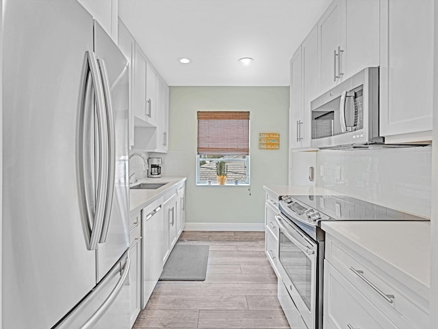 kitchen with appliances with stainless steel finishes, light wood-type flooring, sink, and white cabinets