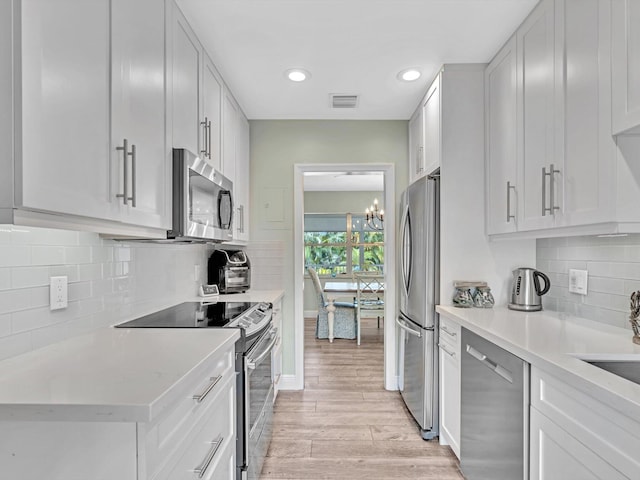 kitchen with backsplash, white cabinetry, stainless steel appliances, an inviting chandelier, and light hardwood / wood-style floors