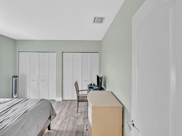 bedroom with a textured ceiling, light wood-type flooring, and two closets