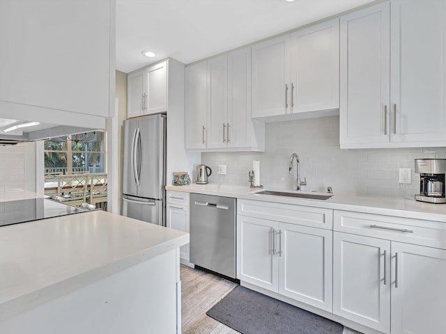 kitchen featuring light wood-type flooring, tasteful backsplash, sink, stainless steel appliances, and white cabinetry