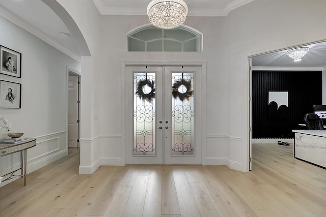 foyer entrance featuring crown molding, light hardwood / wood-style floors, french doors, and a notable chandelier