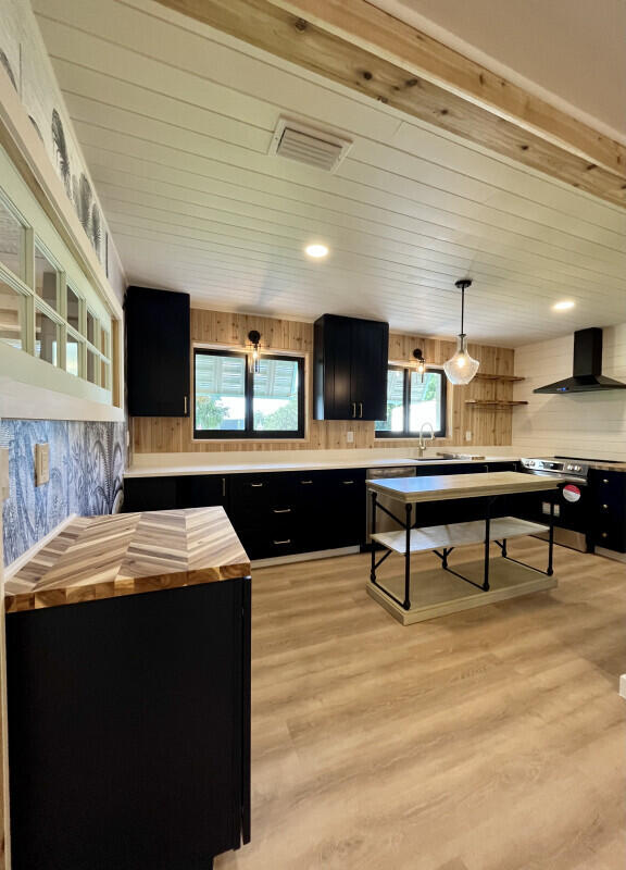 kitchen with sink, decorative light fixtures, wall chimney range hood, stainless steel electric stove, and light wood-type flooring