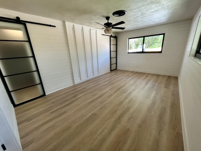 unfurnished bedroom with ceiling fan, light wood-type flooring, and a barn door