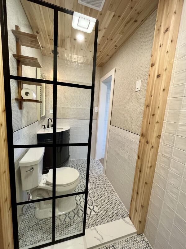 bathroom featuring vanity, a shower, wooden ceiling, tile walls, and toilet