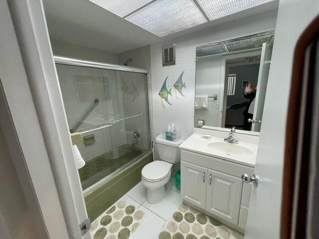 full bathroom with tile patterned floors, bath / shower combo with glass door, vanity, and toilet