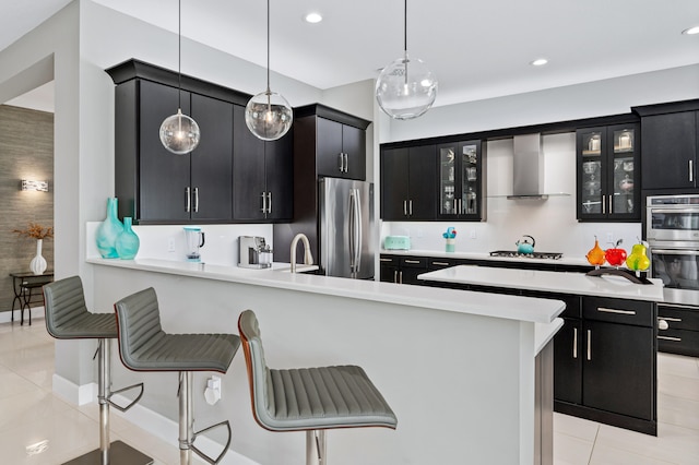 kitchen with light tile patterned flooring, hanging light fixtures, stainless steel appliances, wall chimney exhaust hood, and a breakfast bar