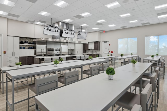 kitchen featuring a drop ceiling, decorative backsplash, light wood-type flooring, and a large island with sink