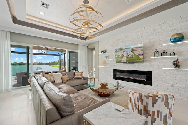 tiled living room with a water view, a tray ceiling, and a chandelier