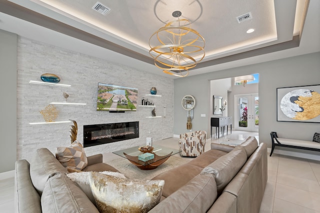 tiled living room featuring a notable chandelier, a fireplace, and a tray ceiling