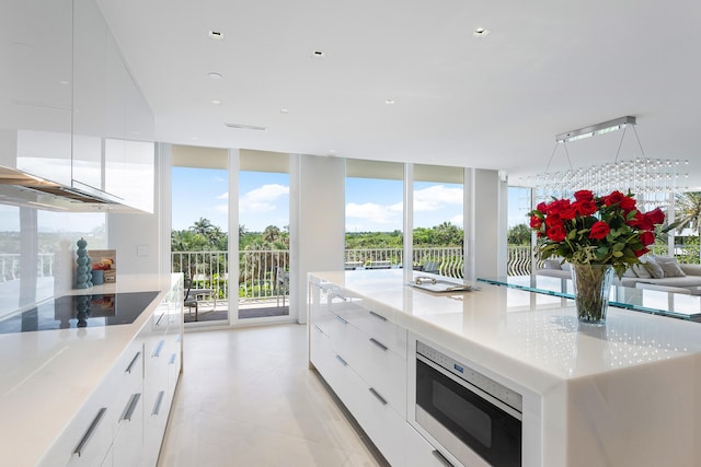 kitchen featuring stainless steel microwave, expansive windows, black electric cooktop, a large island, and white cabinetry