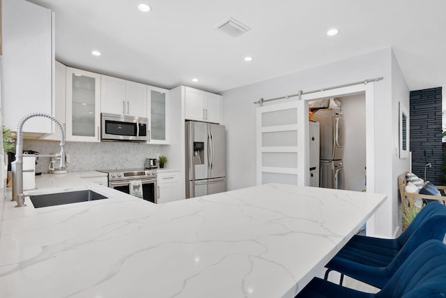 kitchen featuring visible vents, a barn door, a sink, appliances with stainless steel finishes, and stacked washer / drying machine