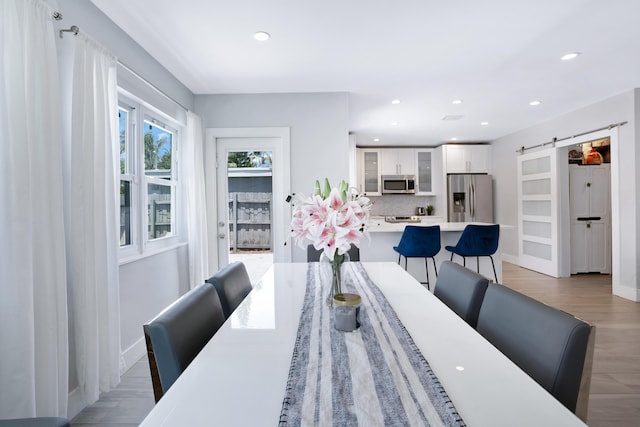 dining room with light wood-style flooring, recessed lighting, baseboards, and a barn door