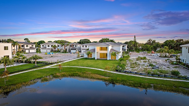 back house at dusk featuring a lawn, a water view, and a garage