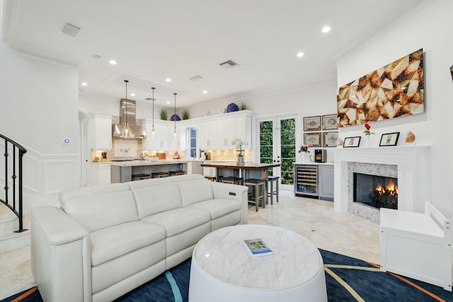 living room with wine cooler, ornamental molding, and a tiled fireplace