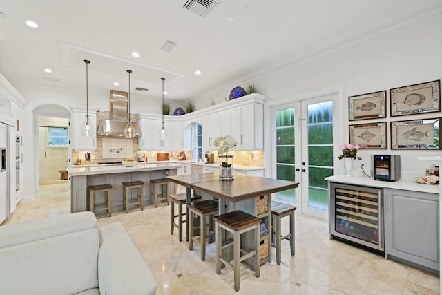 kitchen featuring hanging light fixtures, wall chimney exhaust hood, decorative backsplash, a kitchen island, and white cabinetry