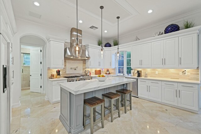 kitchen featuring a center island, wall chimney exhaust hood, decorative light fixtures, white cabinetry, and stainless steel appliances